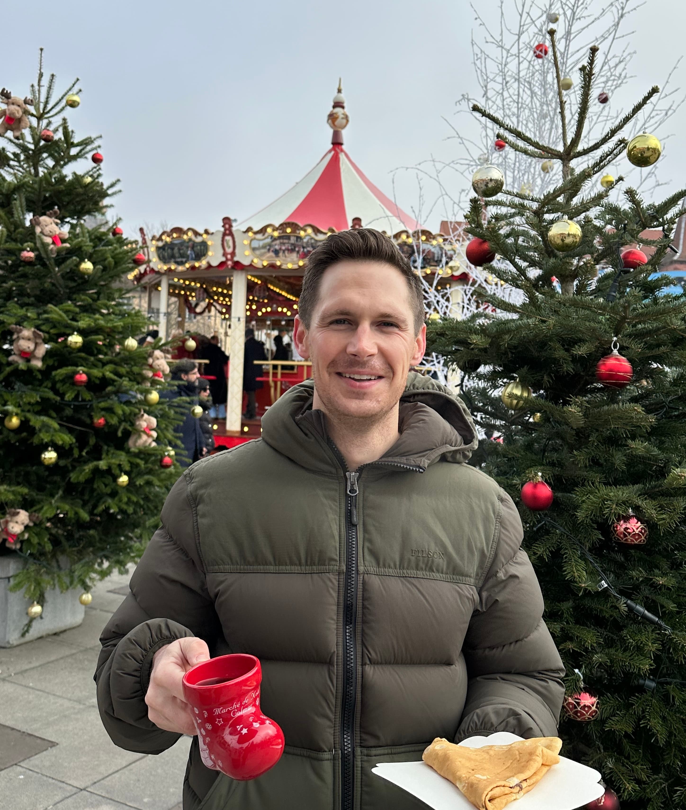 Kyle holding a glass of gluhwein and a crepe in Colmar's Christmas Market.
